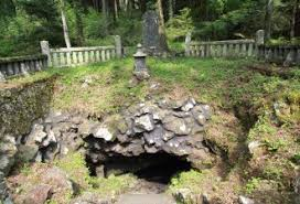 A small shrine with stone steps and a lantern in front of a small cave among rocks