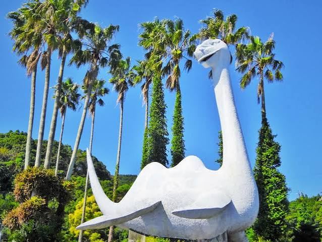A white, plesiosaur-like Issie statue standing between palm trees