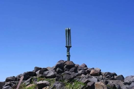 A metal Heavenly Sakahoko spear standing on rocks at the summit of Takachiho-no-mine